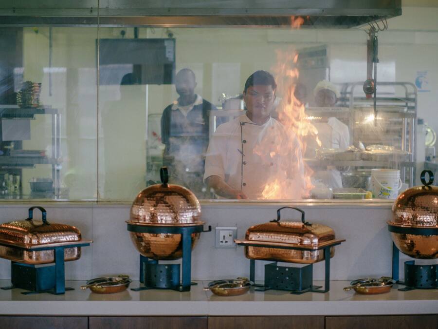 Una cocina con utensilios de cobre y un chef trabajando detrás de un separador de vidrio.