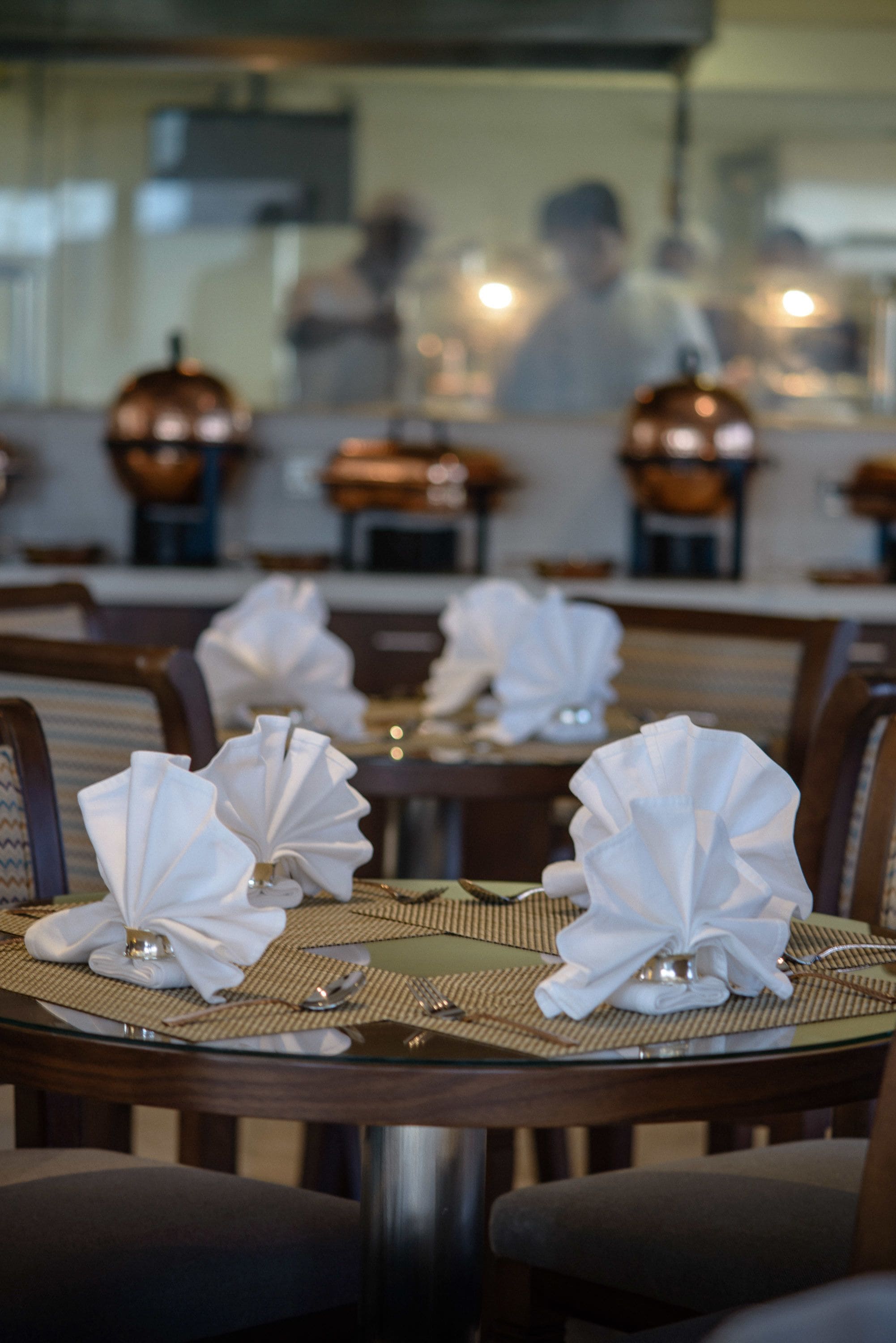Un restaurante con mesas dispuestas, blancas servilletas y cubiertos, y el reflejo de una persona al fondo.