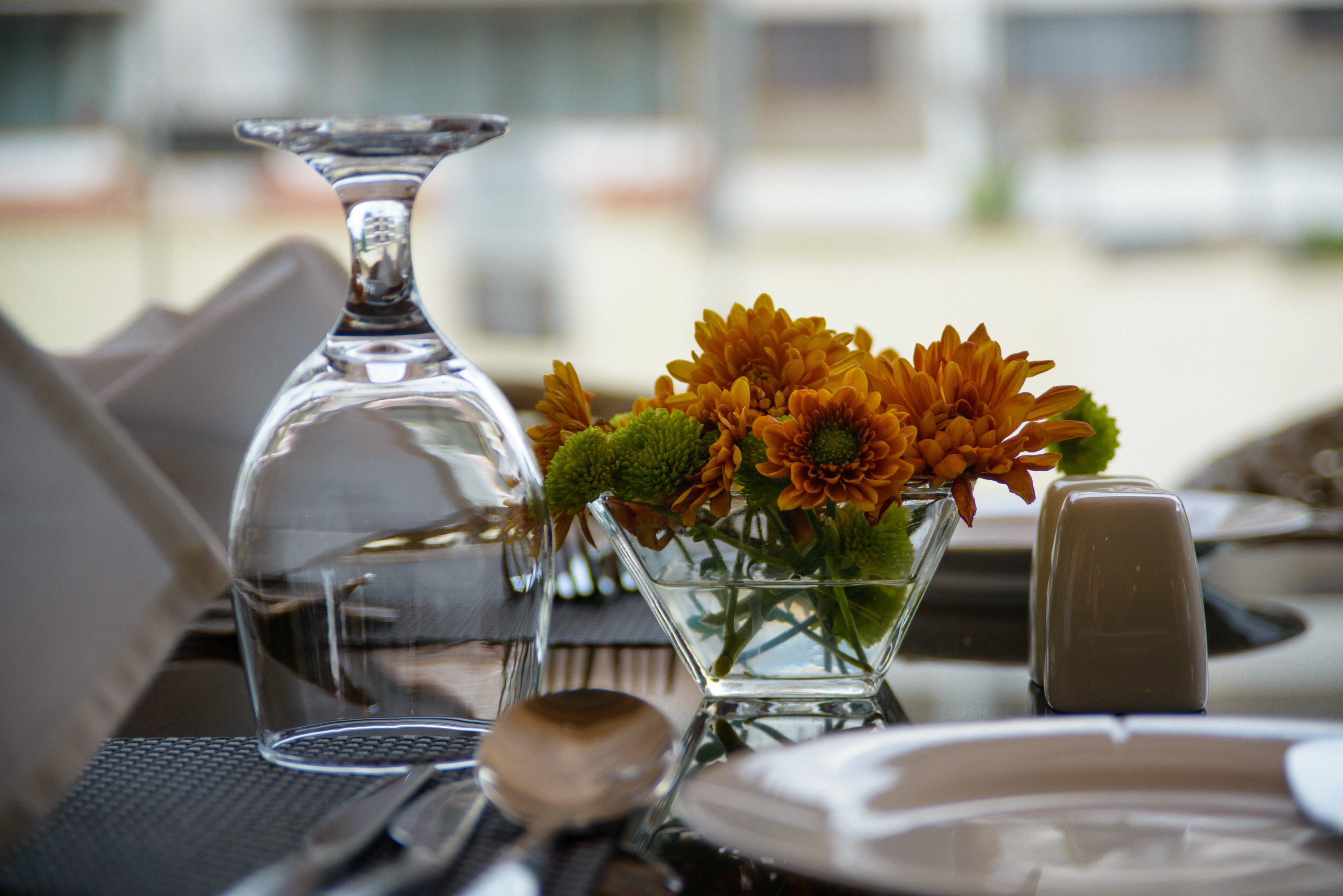 Une table dressée avec un pichet en verre transparent, un vase en verre contenant des fleurs oranges et un salier.