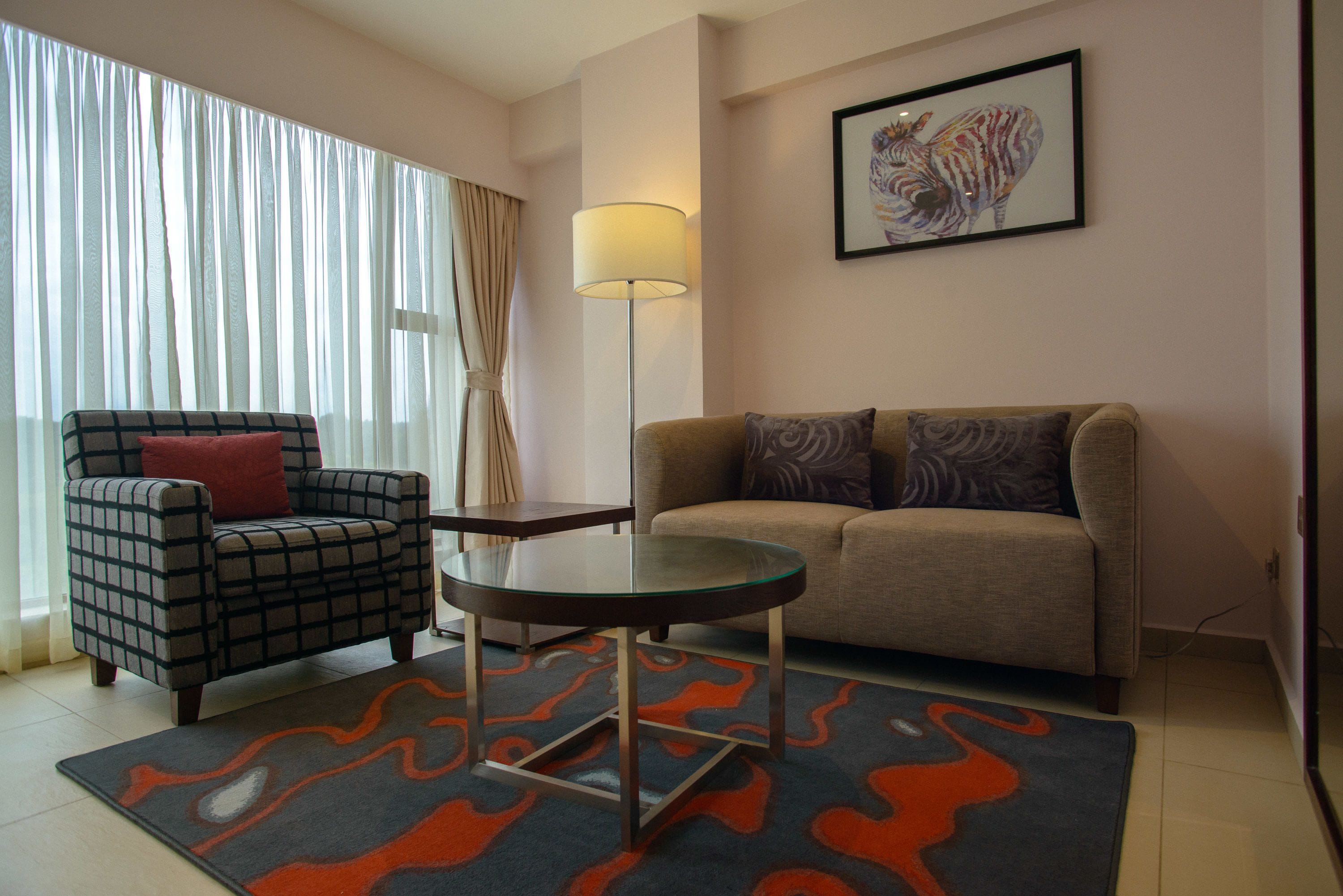 Una sala de estar con un sillón a cuadros, un sofá, una mesa de centro de vidrio y una lámpara de pie.
