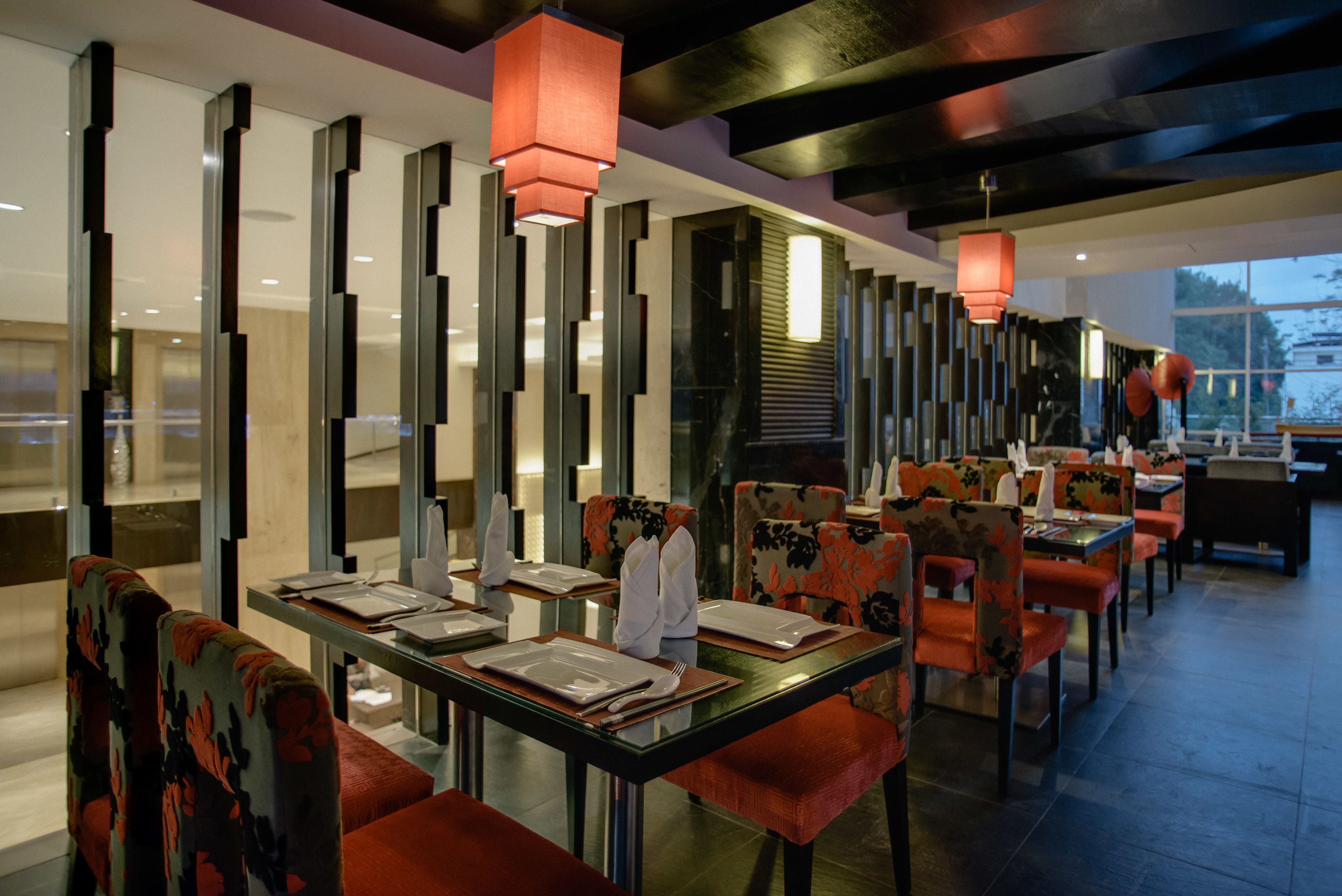 Un restaurante moderno con mesas y sillas de vidrio, cojines rojos y lámparas verticales.