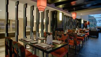 Un restaurante moderno con mesas y sillas de vidrio, cojines rojos y lámparas verticales.