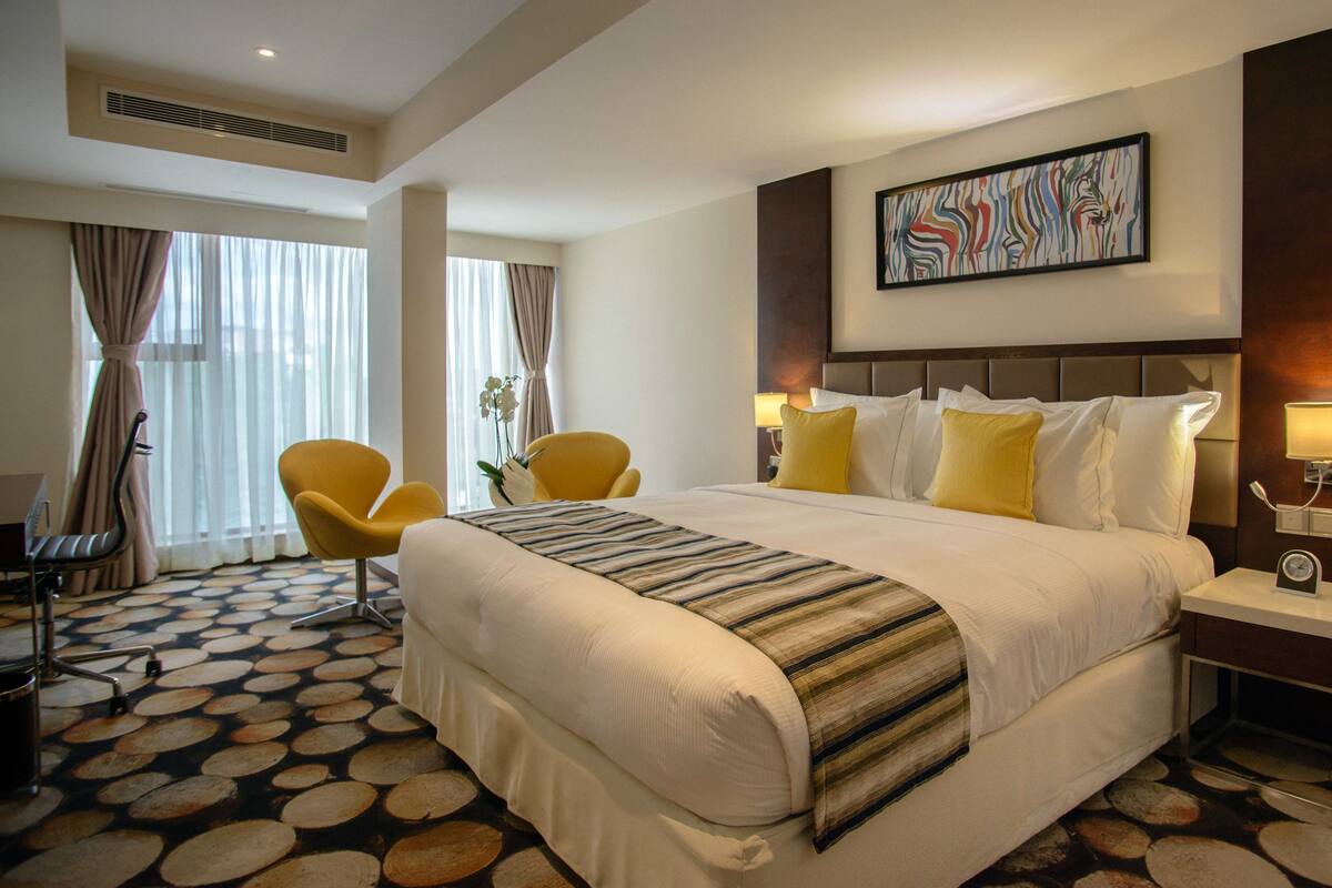 Habitación de hotel con una cama grande, una silla, un escritorio y un ventanal con cortinas.