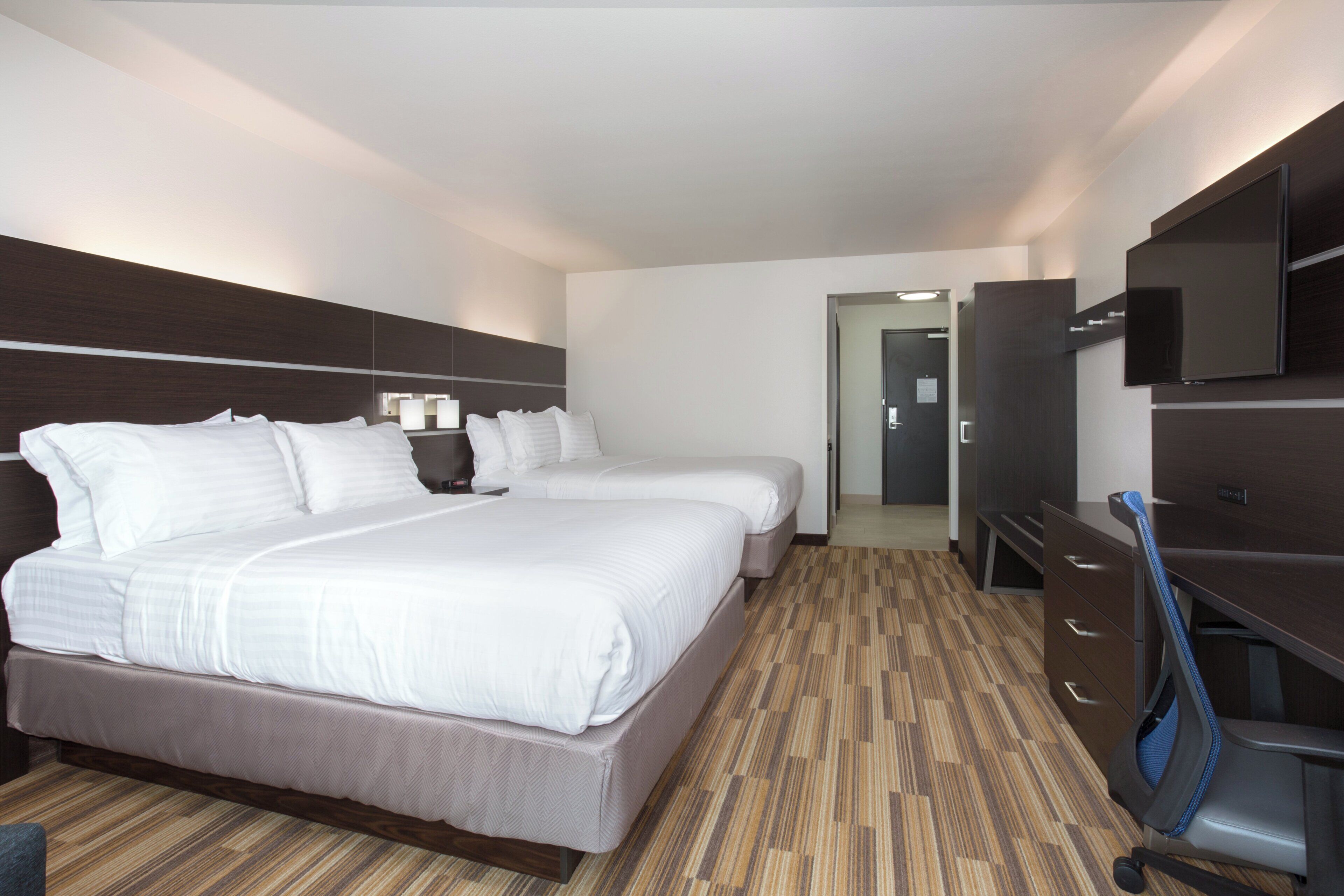 A hotel room with two beds, a desk, a TV, and a wardrobe.