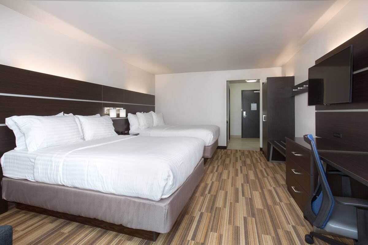 A hotel room with two beds, a desk, a chair, a TV, and a wardrobe.