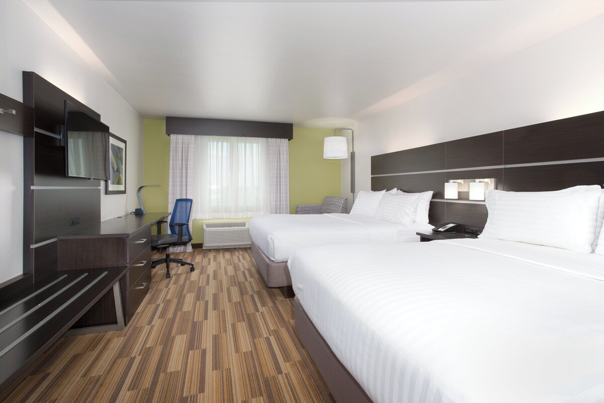 A hotel room with two beds, a desk, a chair, a TV, and a window with curtains.