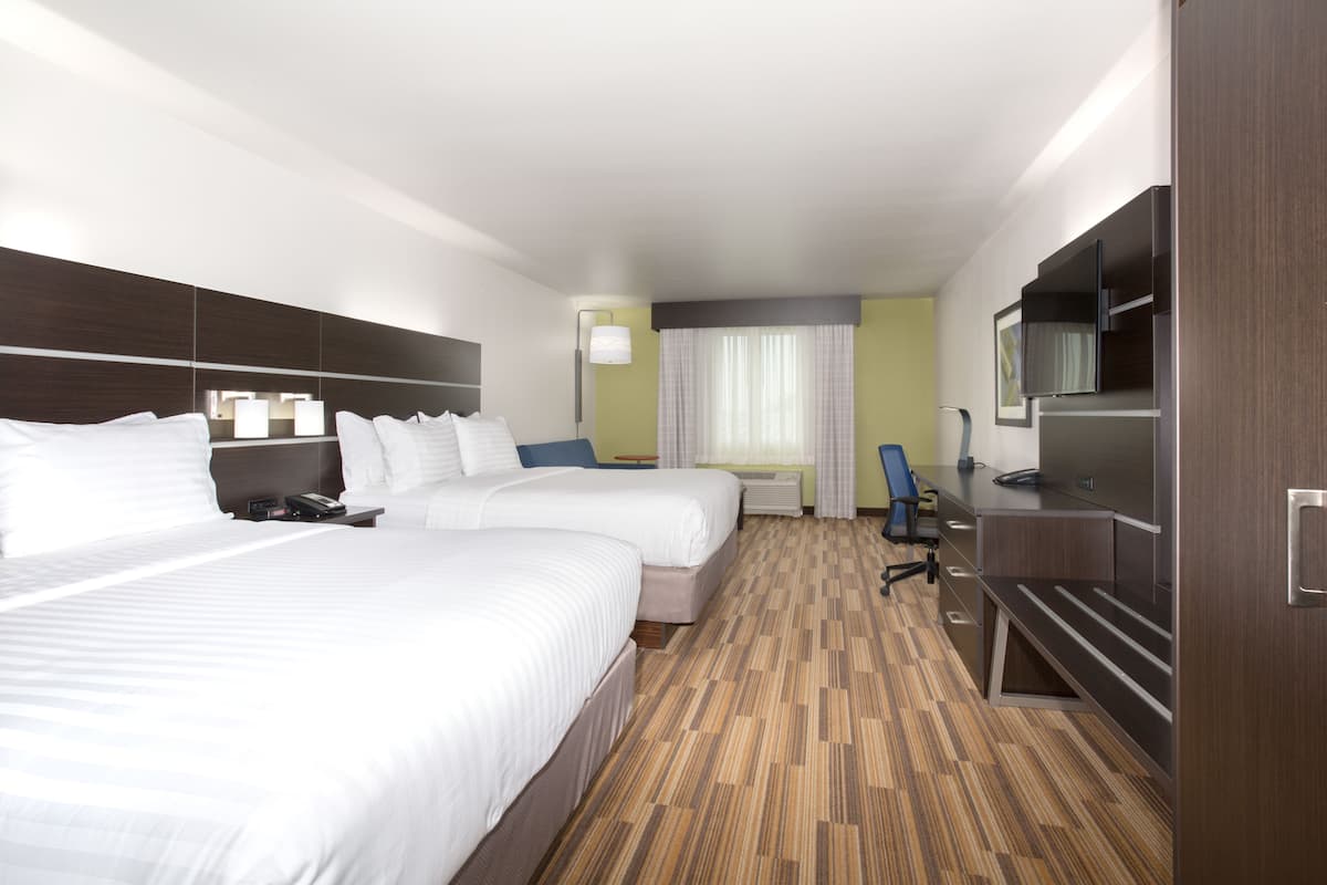A hotel room with two beds, a desk, a chair, a TV, and a window with curtains.