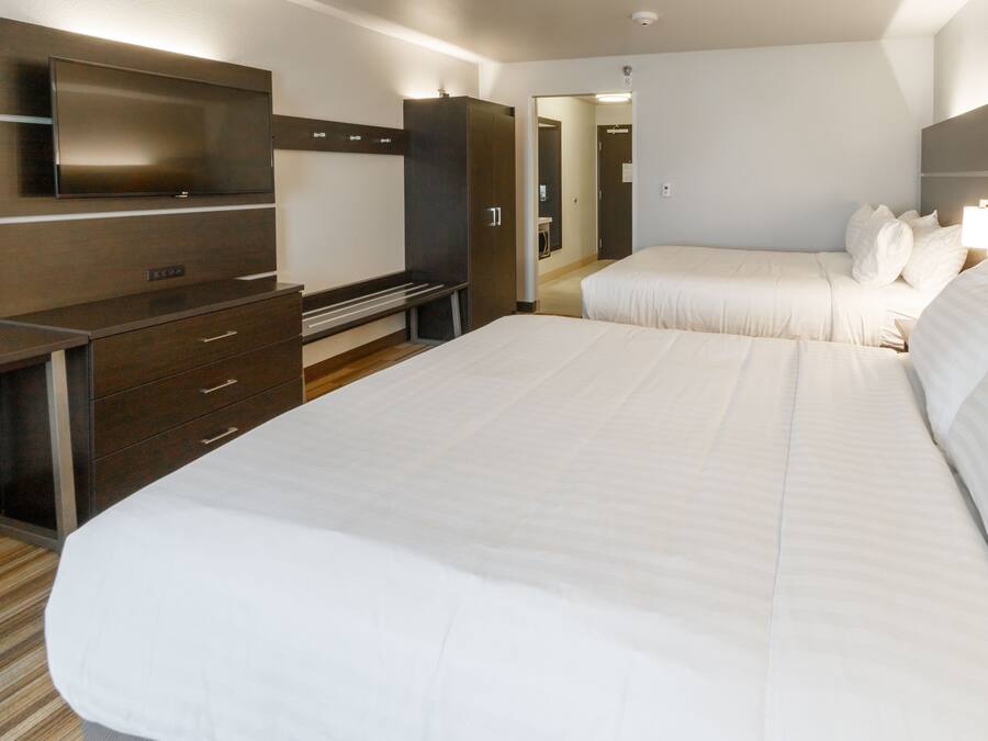 Et hotelværelse med en stor seng, et fjernsyn ophængt på væggen, et skrivebord og et klædeskab.