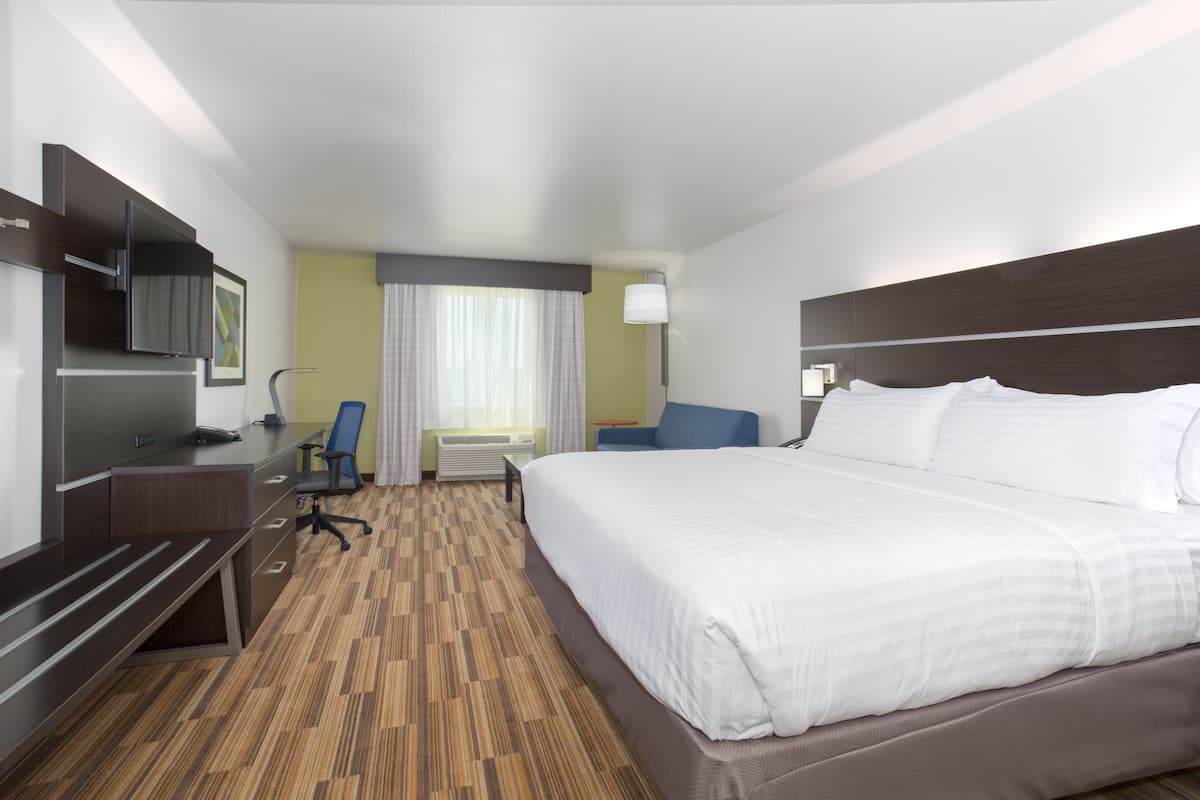 A hotel room with a large bed, a desk with a chair, a television, and a window with curtains.