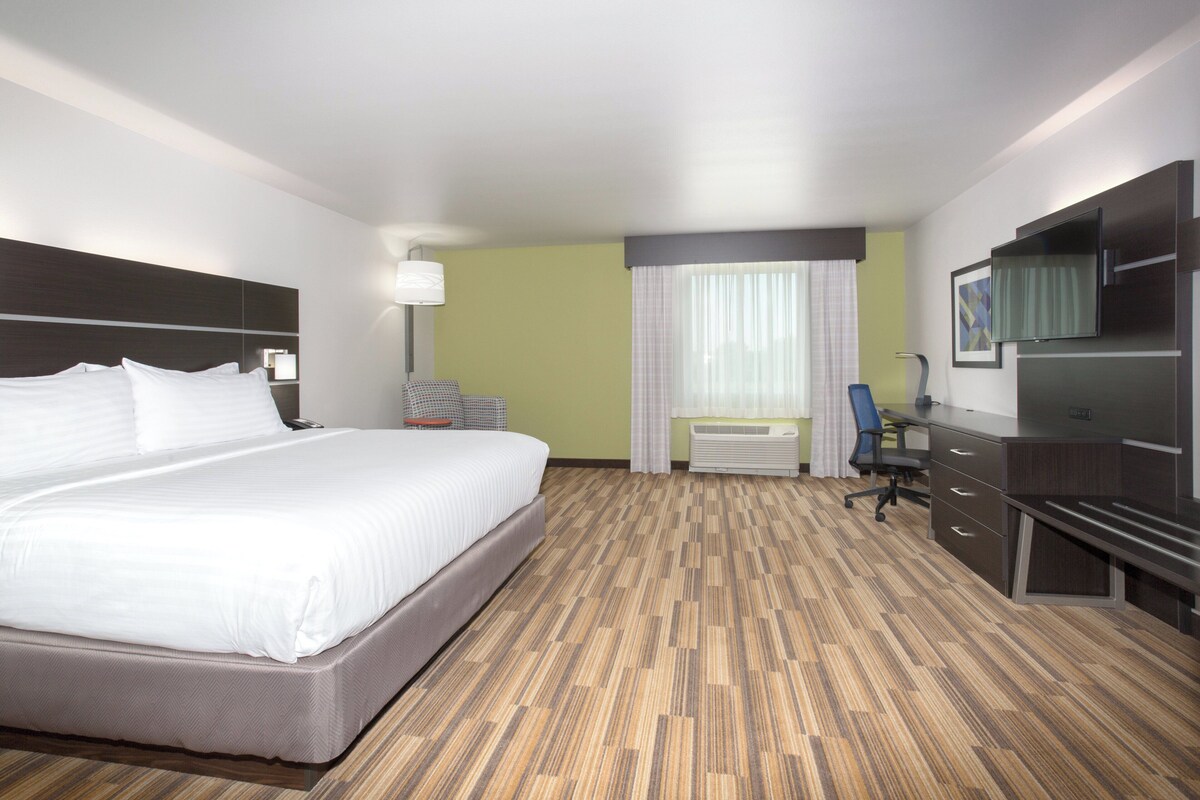 A hotel room with a large bed, a desk, a chair, a TV, and a window with curtains.