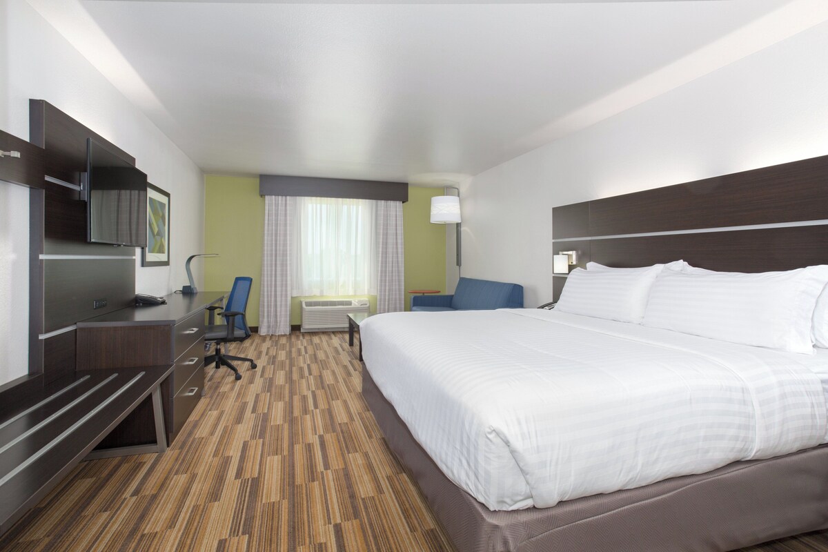 A hotel room with a large bed, a desk with a chair, a television, and a window with curtains.