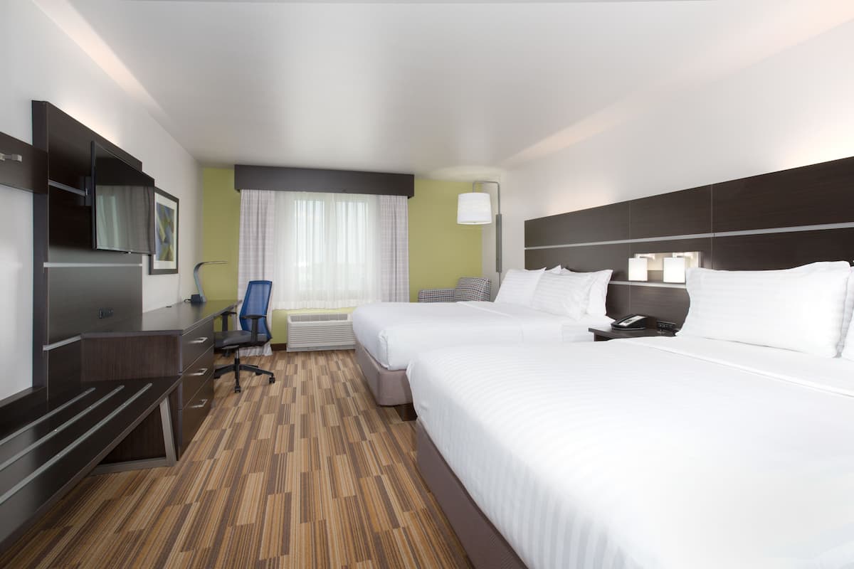 A hotel room with two beds, a desk, a chair, a TV, and a window with curtains.