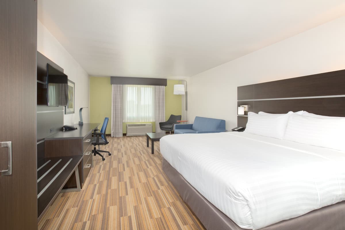 A hotel room with a large bed, a desk, a chair, a TV, and a window with curtains.