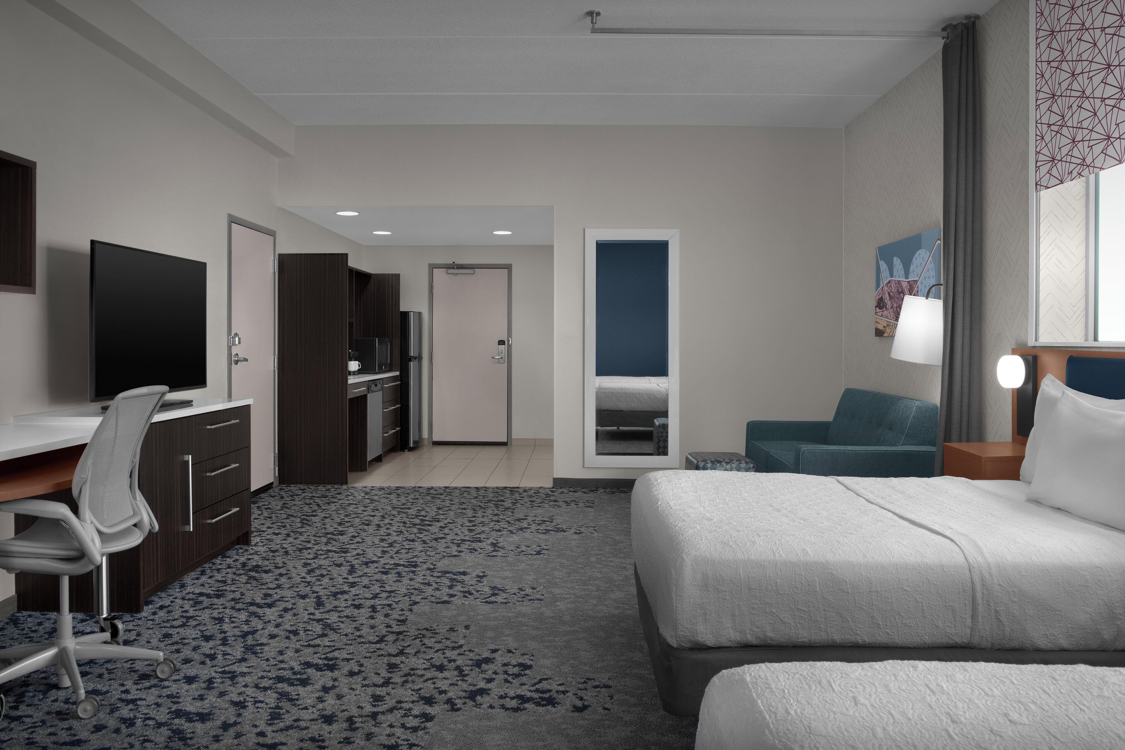 A hotel room with a bed, desk, chair, and a television.
