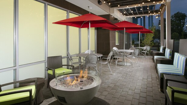 Une terrasse extérieure aménagée avec des meubles en osier, des parasols rouges et un foyer.