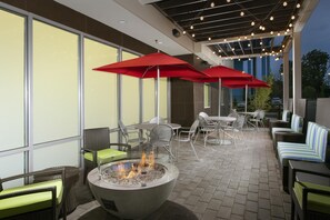 An outdoor patio with wicker furniture, red umbrellas, and a fire pit.