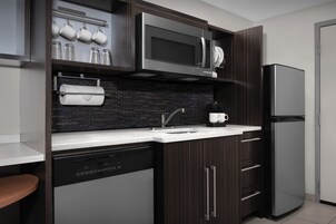 Una cocina moderna con lavavajillas, electrodomésticos de acero inoxidable, salpicadero de azulejos negros y armarios de madera oscura.