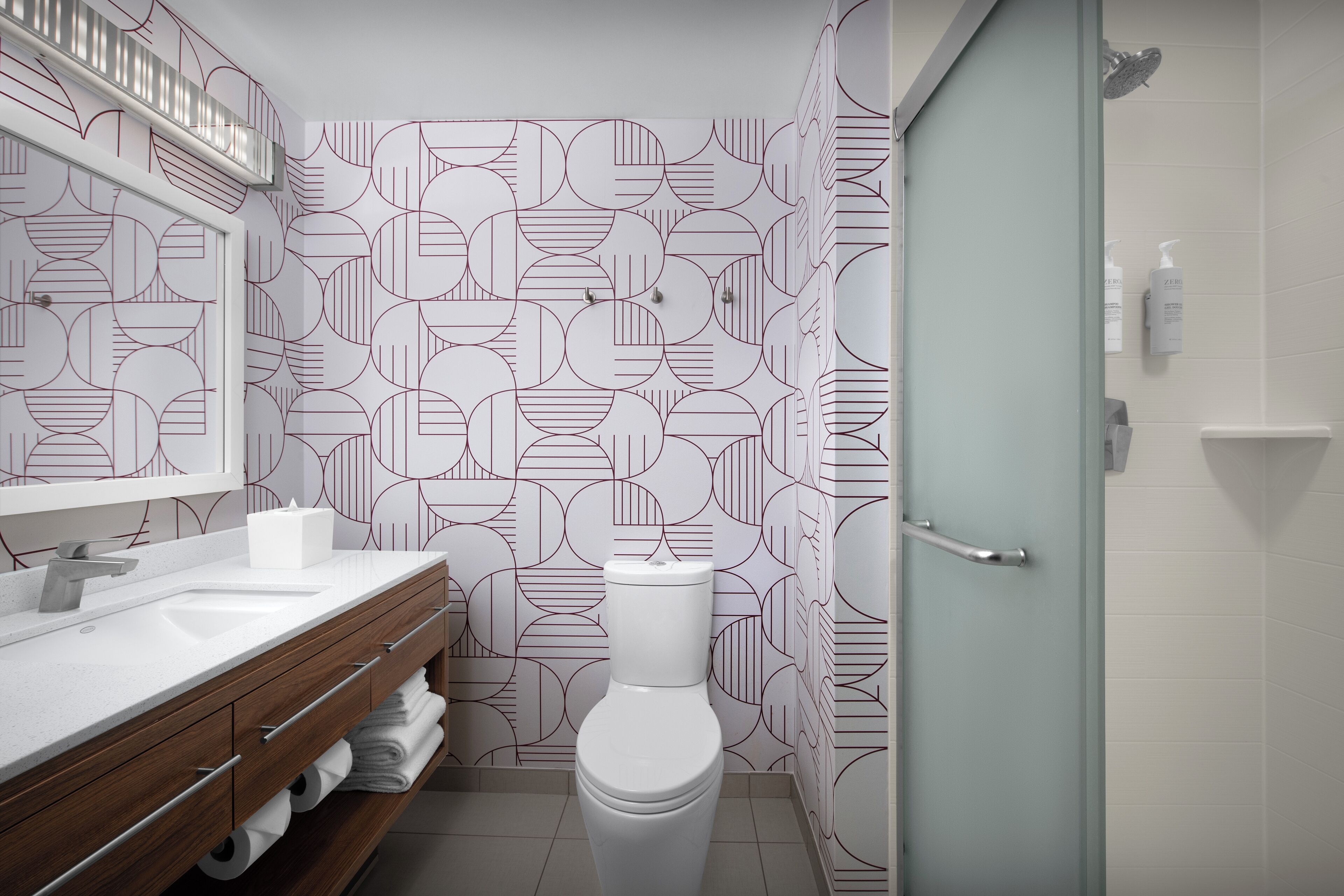 A modern bathroom with a geometric patterned wall, a white sink with a mirror, and a toilet.