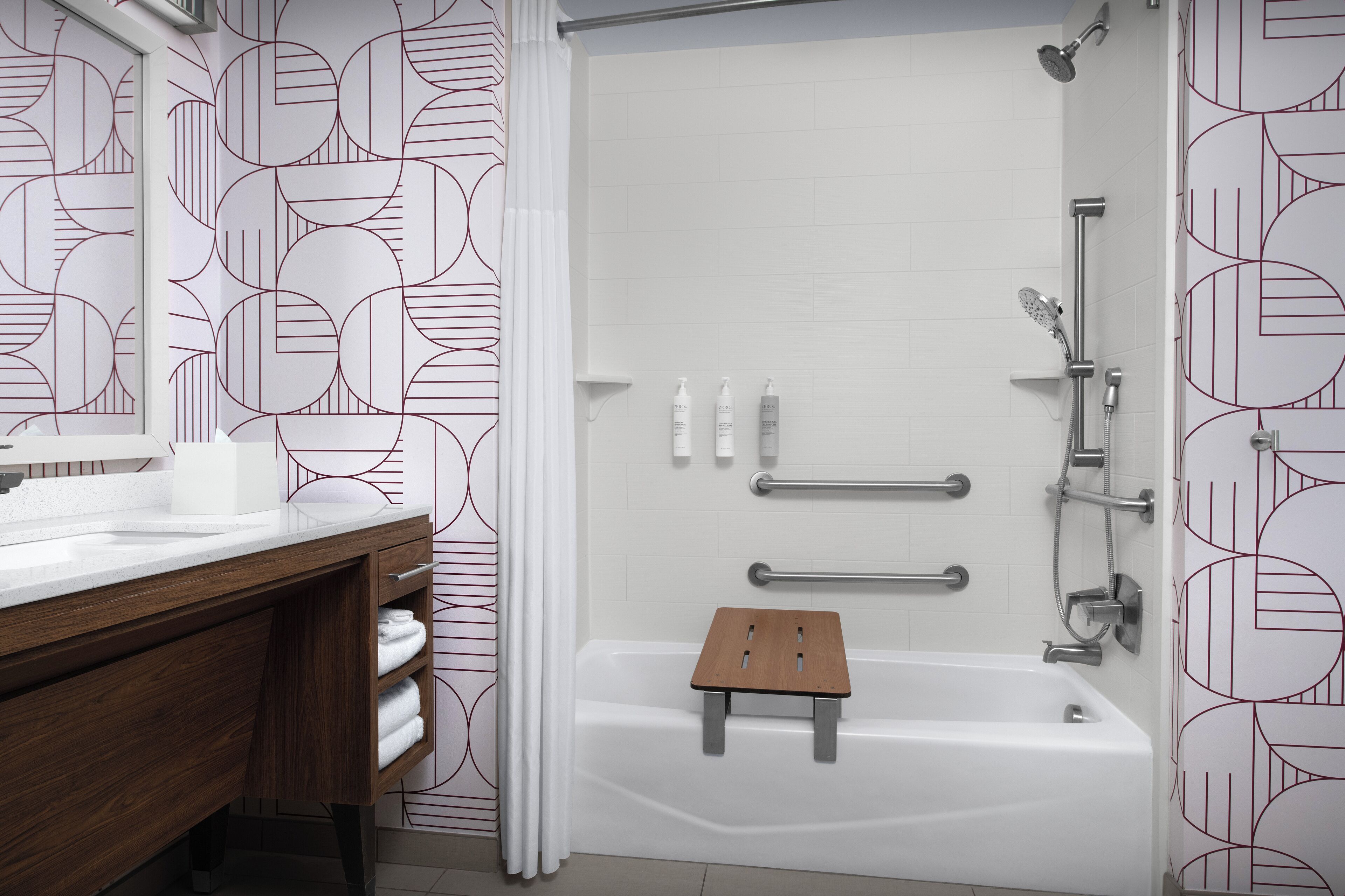 A modern bathroom with a white bathtub, a wooden stool, and a shower area.