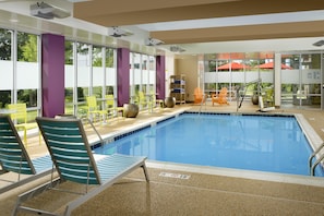 A swimming pool with lounge chairs and tables, surrounded by large windows and a view of the outdoors. - Home2 Suites by Hilton Arundel Mills/BWI Airport (Hanover)