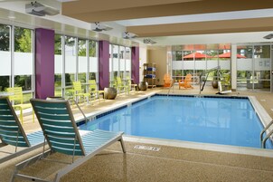 Una piscina con sillones y mesas, rodeada de amplias ventanas y vistas al exterior.
