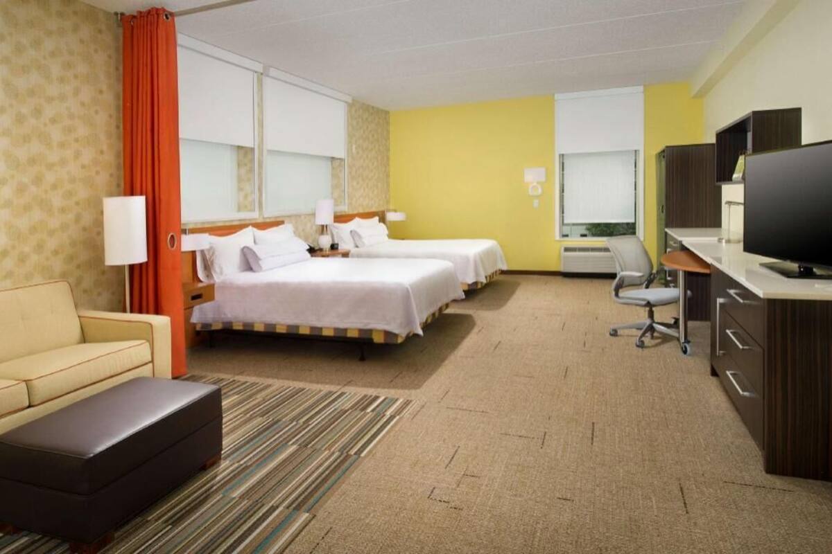 Habitació d'hotel amb dos llits, una escriptori amb un ordinador, un televisor, un sofà i una taula petita.