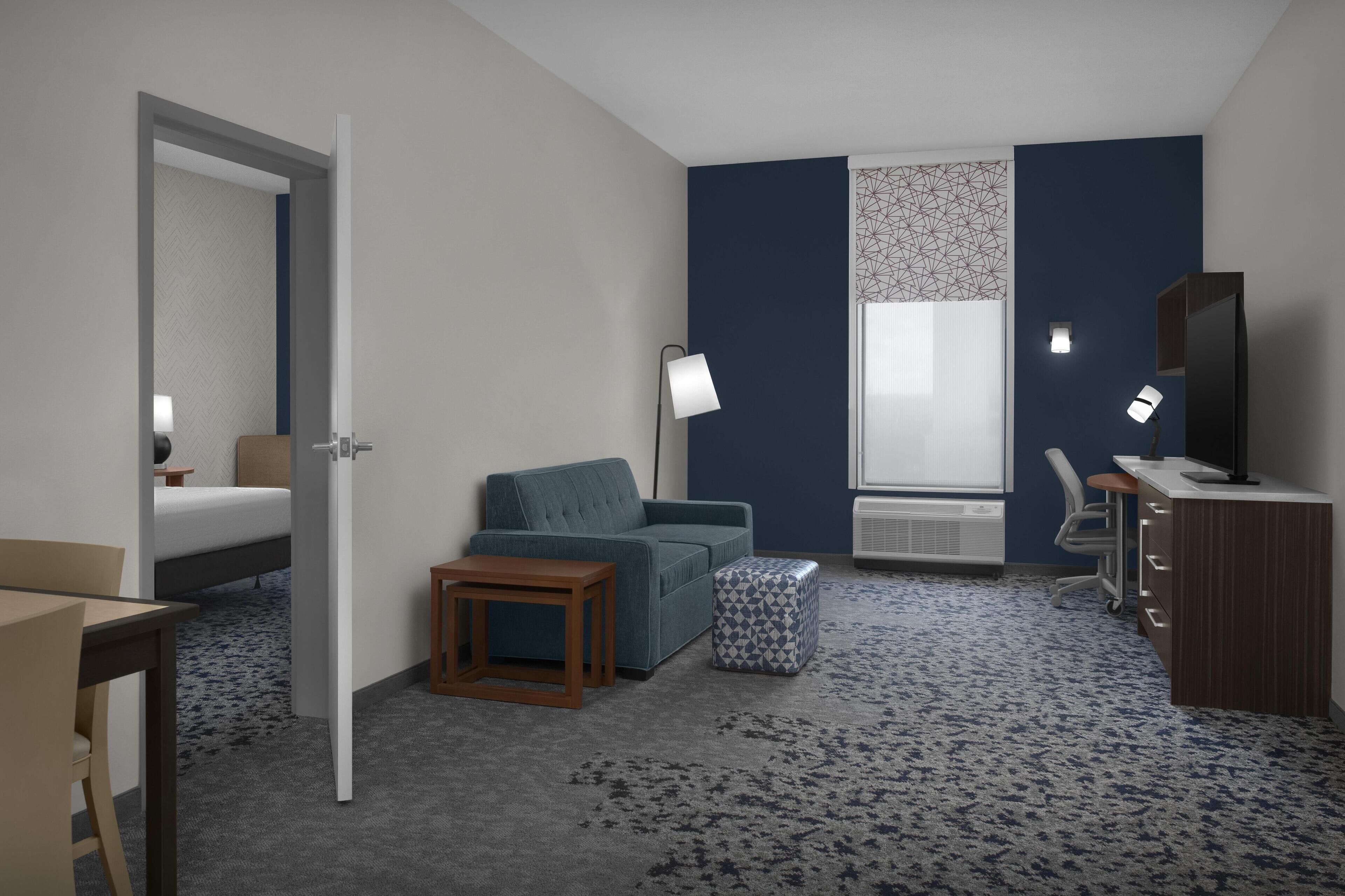 Una habitación de hotel con una cama, un sofá, una mesita, una lámpara, un escritorio y una silla.
