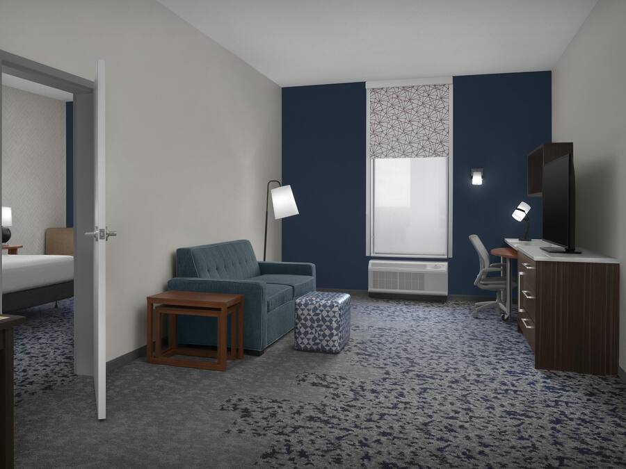 Una habitación de hotel con una cama, un sofá, una mesita, una lámpara, un escritorio y una silla.