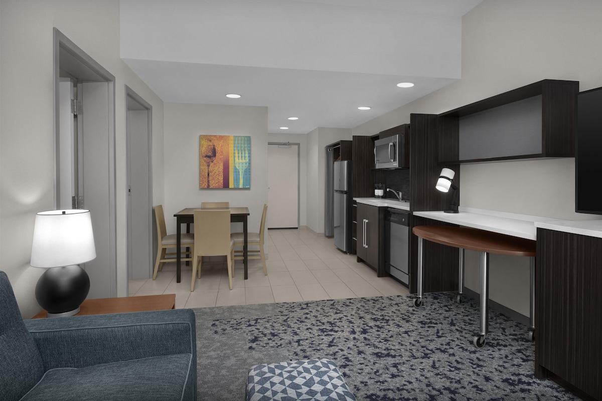 Una cocina moderna con gabinetes oscuros, una encimera blanca y una zona de comedor con mesa y sillas.
