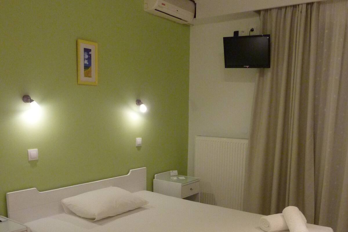 A neatly made bed with white linens, a bedside table with a lamp, and a wall-mounted TV.