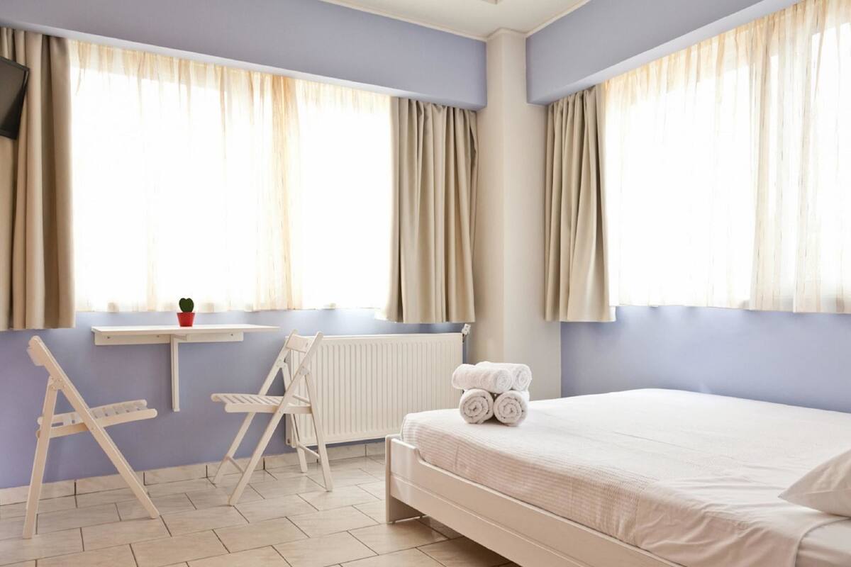 A hotel room with a bed, a chair, a small table, and a window with curtains.