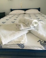 Una cama bien tendida con edredón blanco y dos almohadas, cabecera azul y un enchufe sobre la cama.