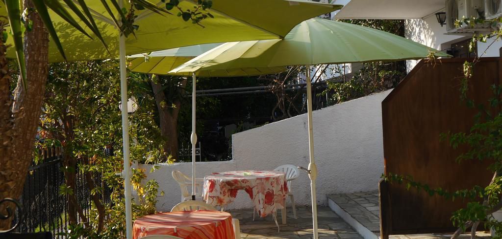 Une terrasse extérieure avec des tables et des chaises sous des parasols, entourée de verdure et d’un mur blanc.