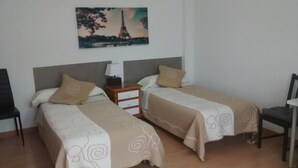 A hotel room with two single beds, a nightstand with a lamp, a chair, and a painting of the Eiffel Tower on the wall. - Pensión Santa Rita (Santiago de Compostela)