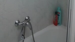 A shower area with a glass door, a handheld showerhead, and a handheld faucet. There are two bottles of shampoo and conditioner on the floor. - Pensión Santa Rita (Santiago de Compostela)