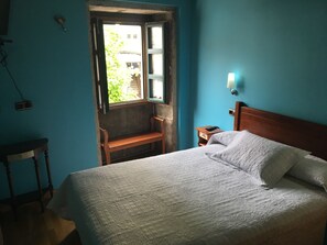 Une chambre avec un lit en bois, un banc près de la fenêtre et une table de chevet avec une lampe.