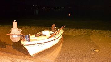 A small boat with a motor and a light on the shore at night.