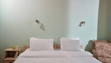 Una cama con ropa blanca, una mesita de noche con una taza y una manzana, y una silla con estampado floral.