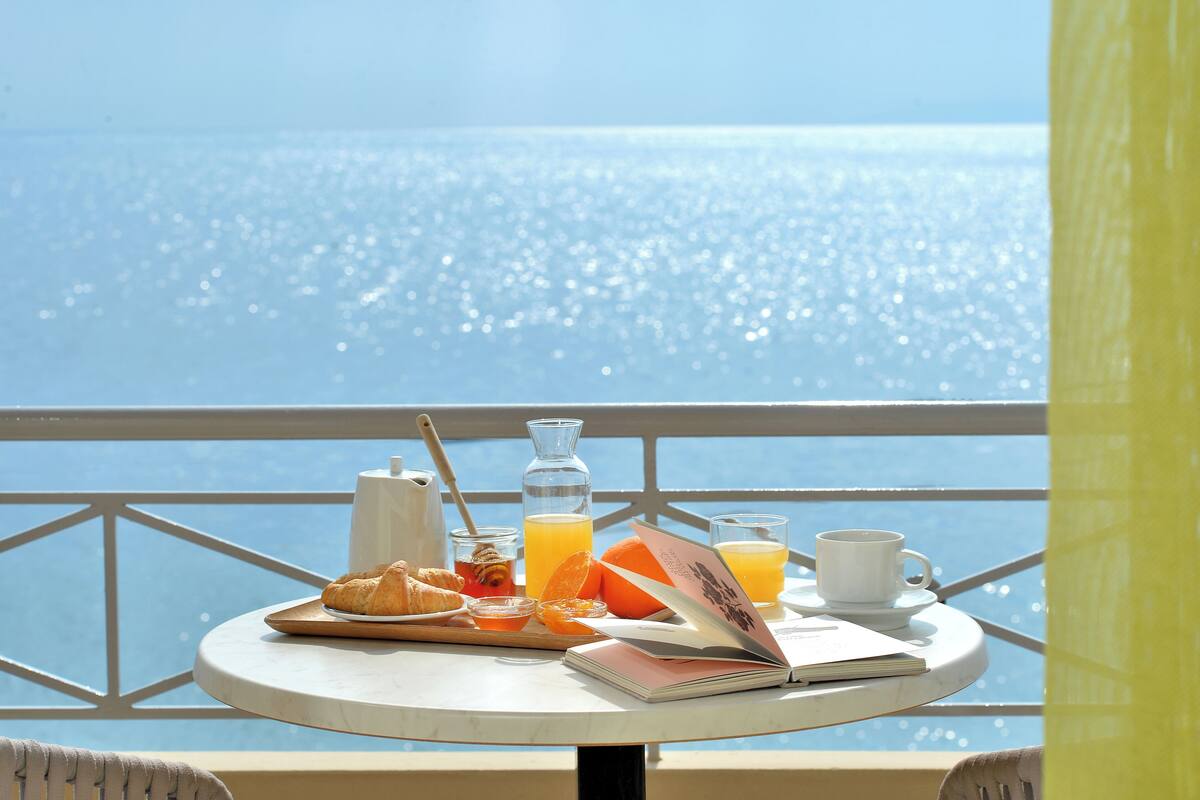 A table with breakfast items and a book, overlooking a body of water.