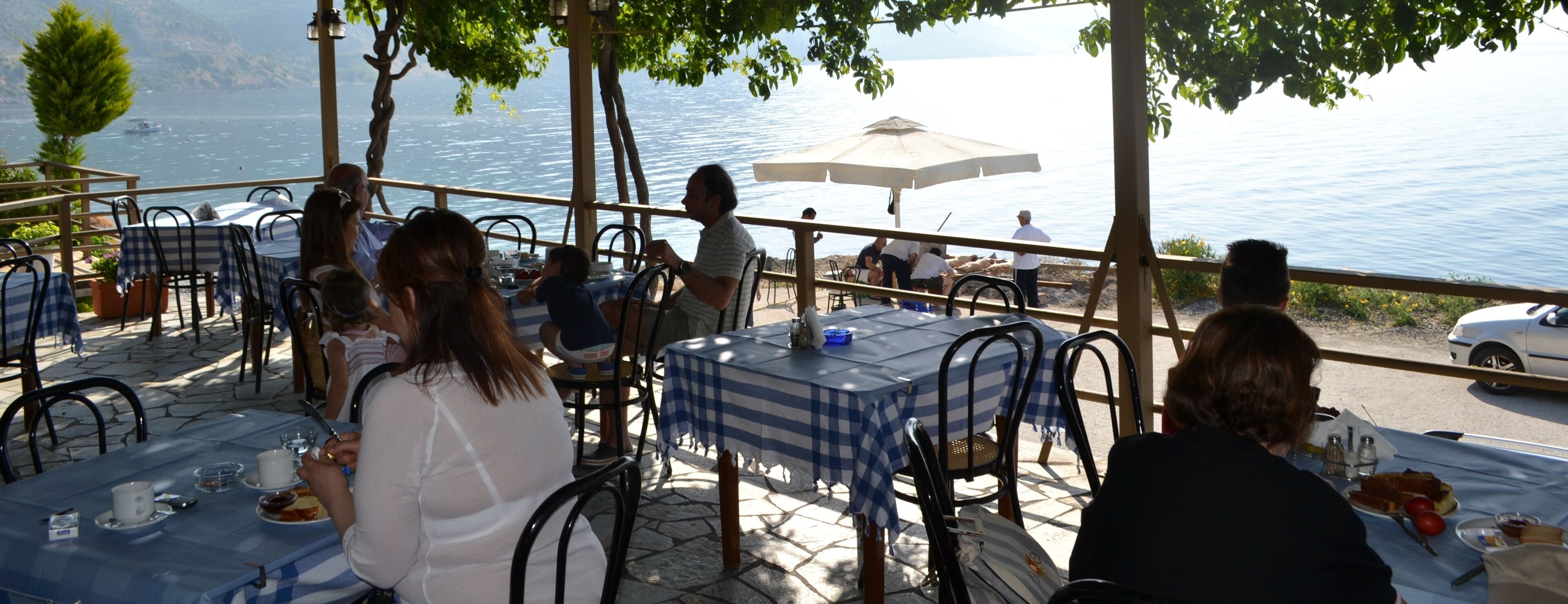 Zona de comedor al aire libre con mesas y sillas, con vista a un cuerpo de agua.
