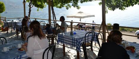 Zona de comedor al aire libre con mesas y sillas, con vista a un cuerpo de agua.