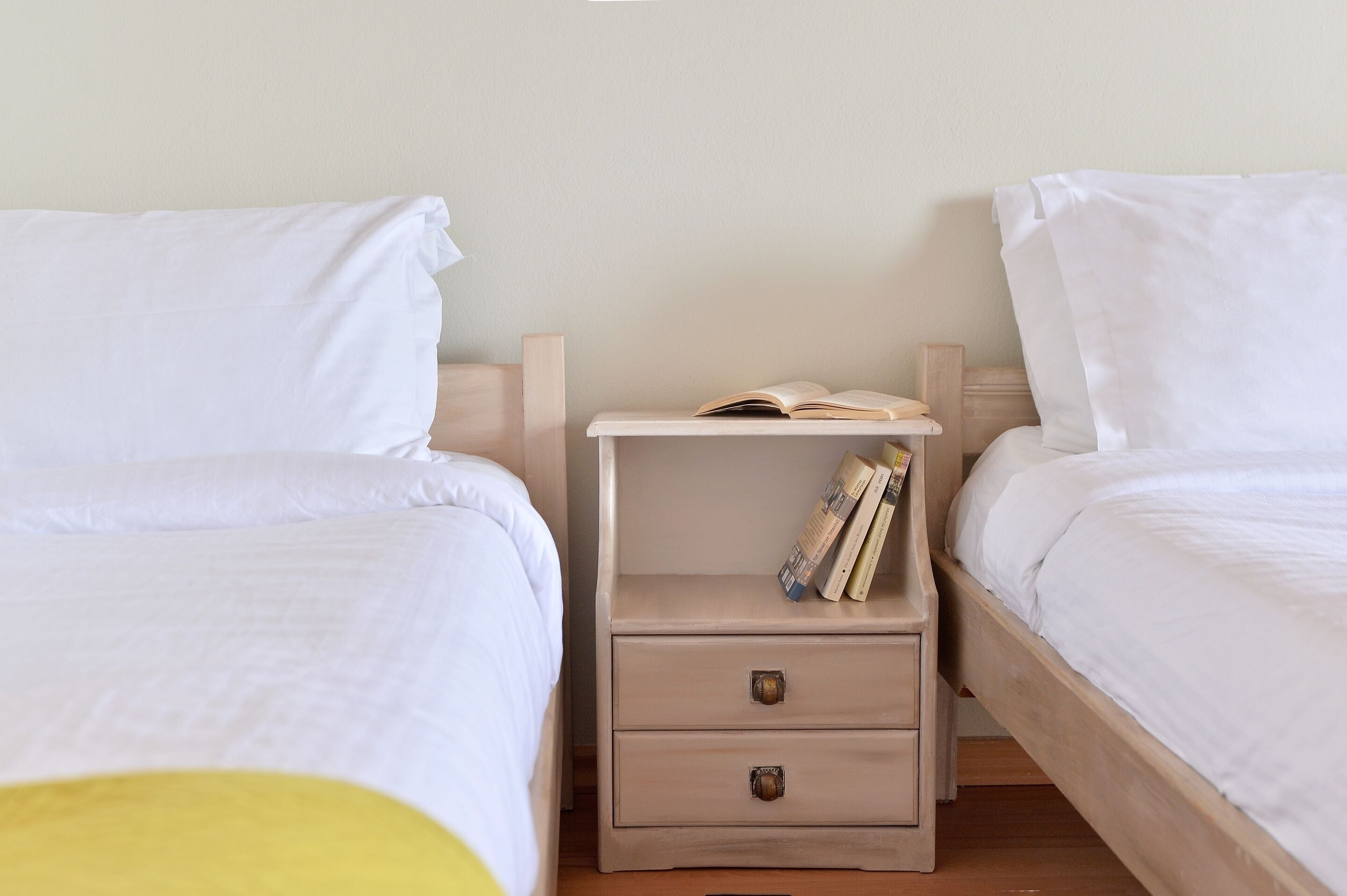 A bedroom with two beds, a nightstand with a book, and a drawer.