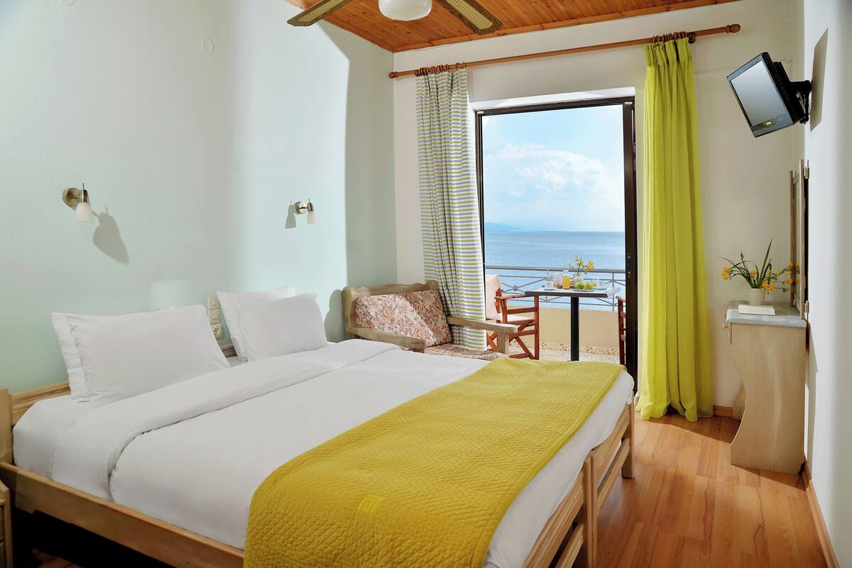 A bedroom with a bed, a desk, a chair, a television, and a view of the sea.