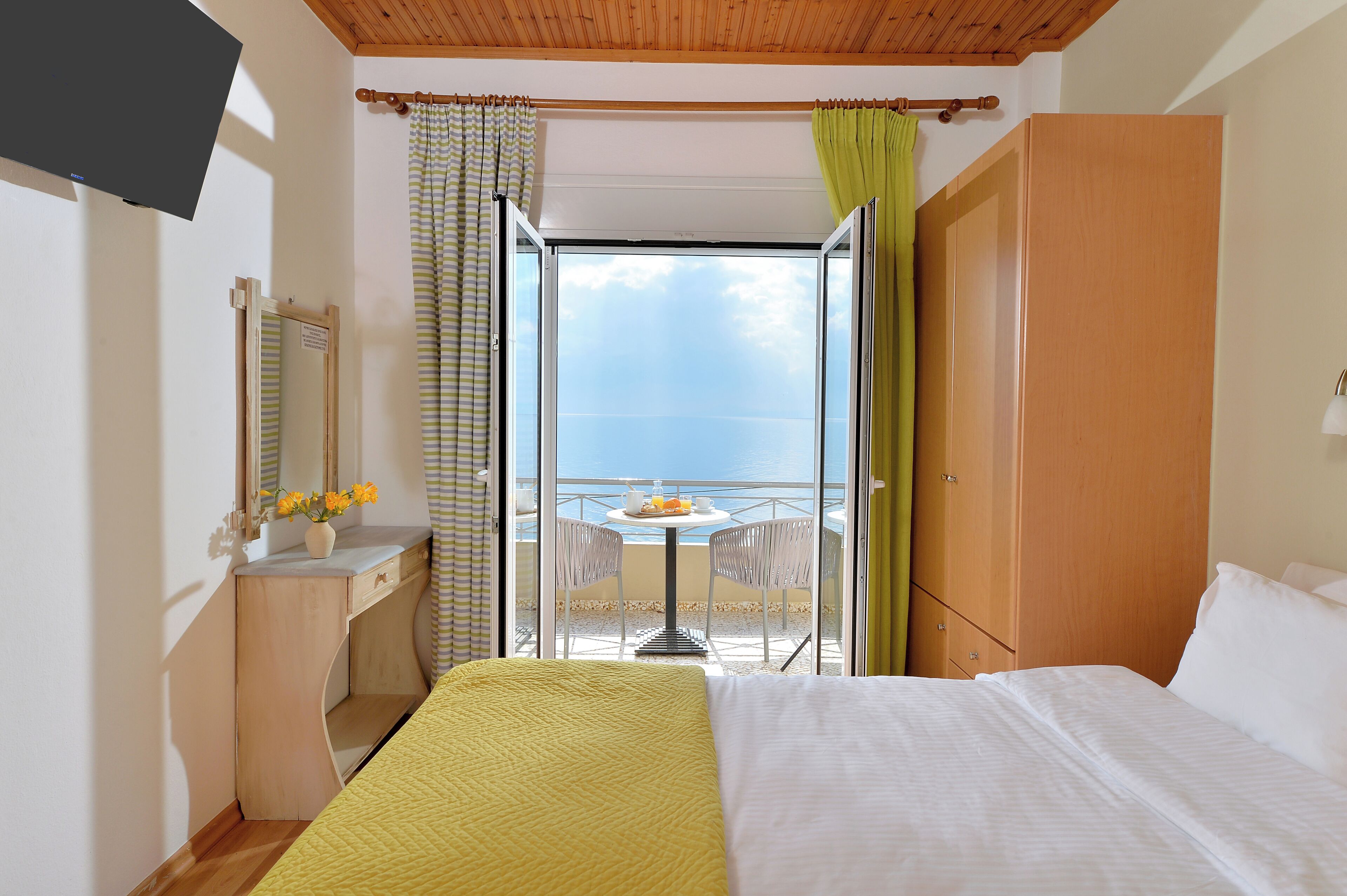 Ein Hotelzimmer mit einem Bett, einem Schreibtisch mit Spiegel, einem kleinen Tisch mit Stuhl sowie einem Balkon mit Tisch und Stühlen.