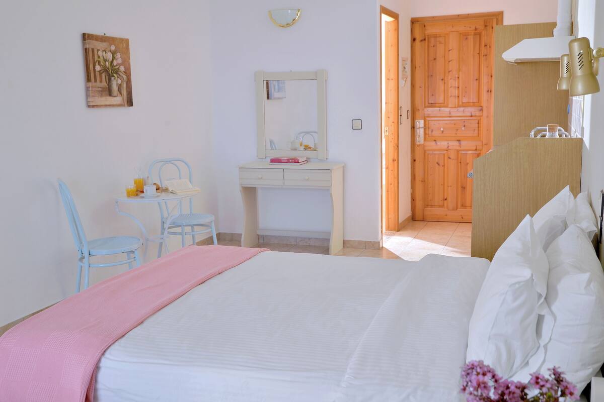 A bedroom with a bed, a desk, a chair, a mirror, and a door.