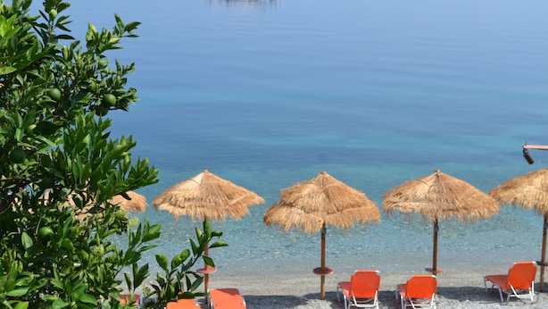 A beach with thatched umbrellas, orange chairs, and a boat in the distance. - Pharos Rooms (Istiaia-Aidipsos)
