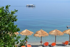 A beach with thatched umbrellas, orange chairs, and a boat in the distance. - Pharos Rooms (Istiaia-Aidipsos)