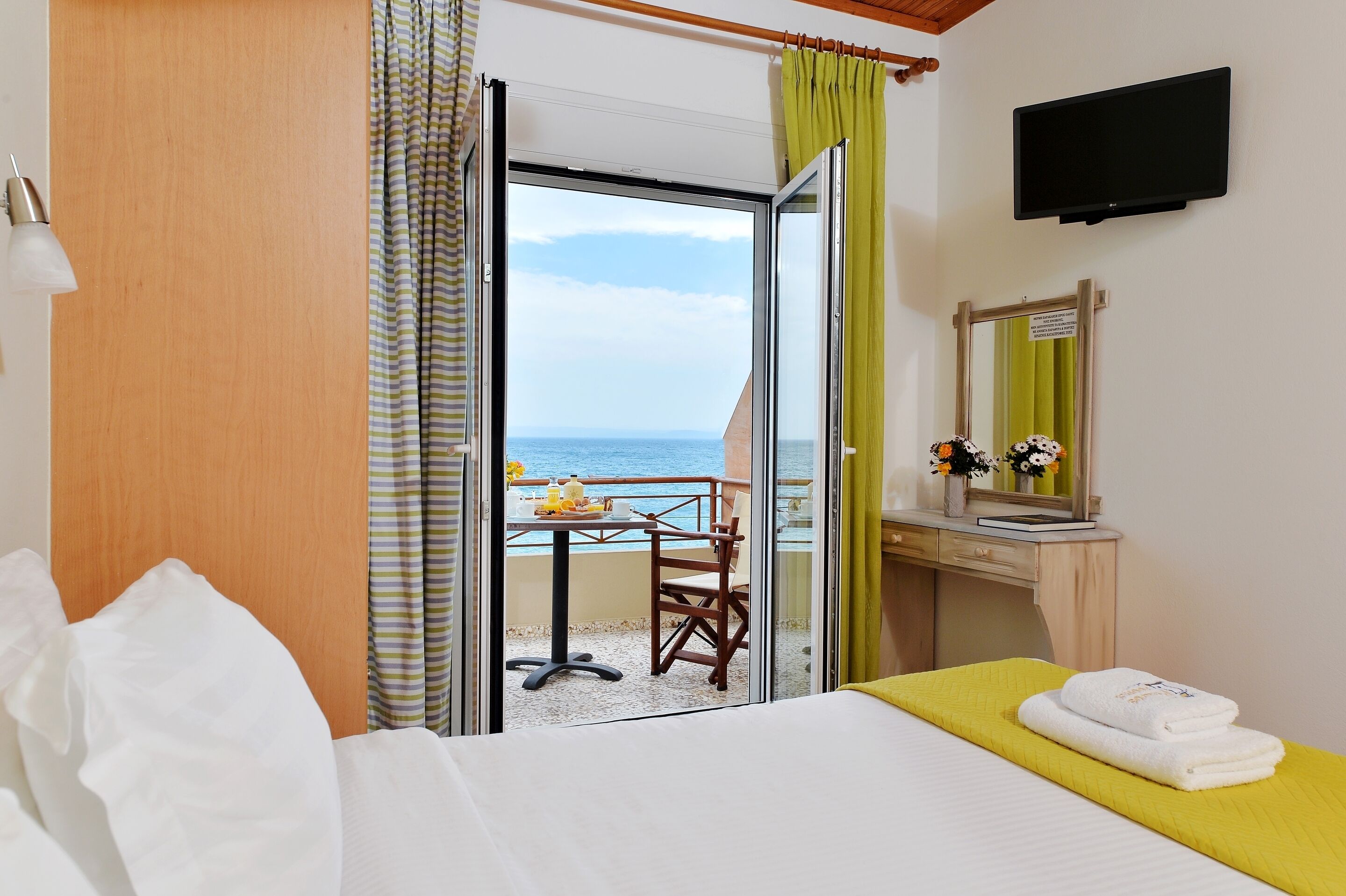 Habitación de hotel con cama, escritorio, televisor y balcón con vista al mar.