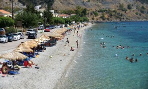 A beach with thatched umbrellas, a hotel, and people swimming in the water. - Pharos Rooms (Istiaia-Aidipsos)