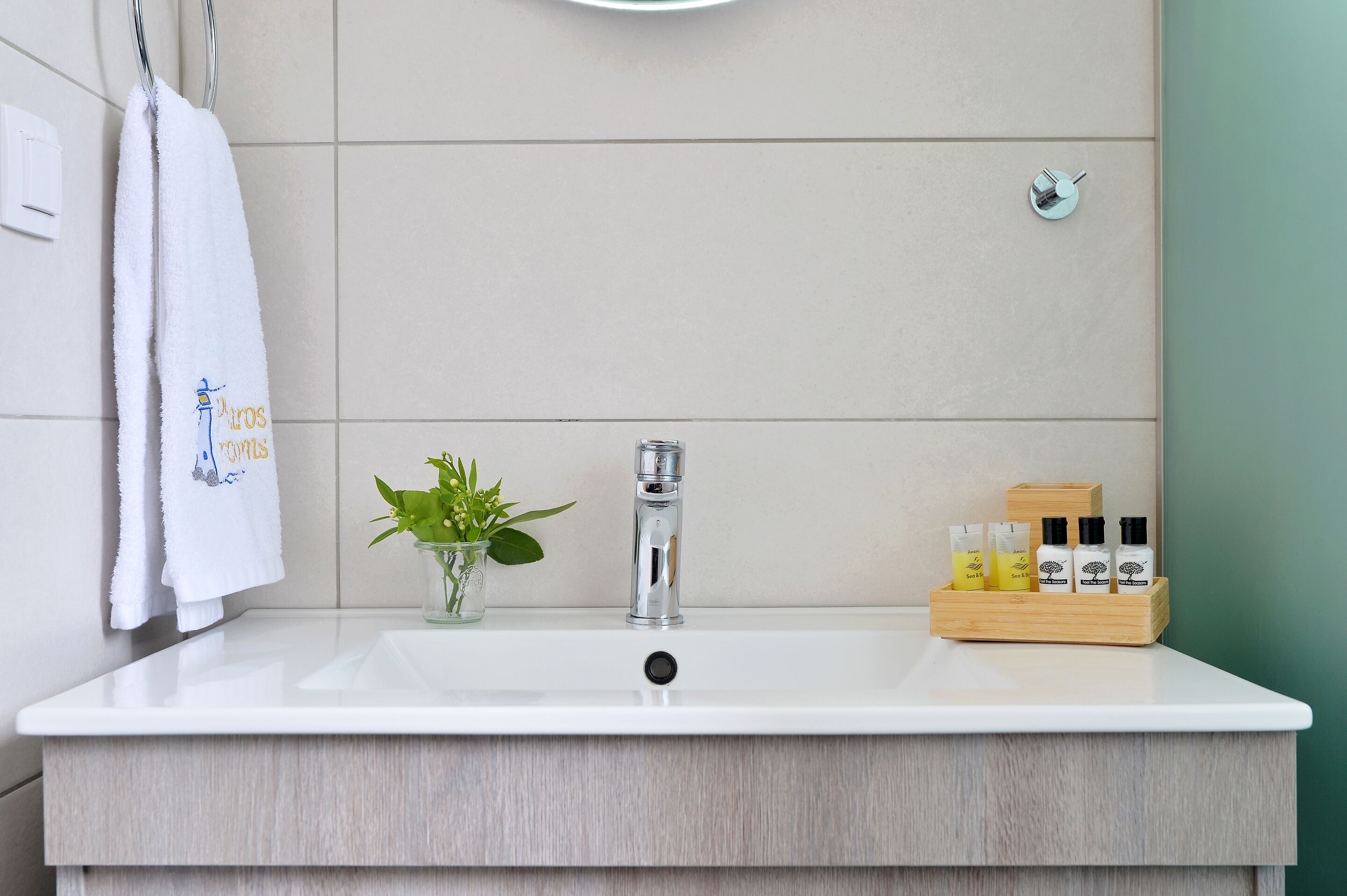 A bathroom with a white sink, a mirror, a towel rack, a potted plant, and a wooden tray with toiletries.